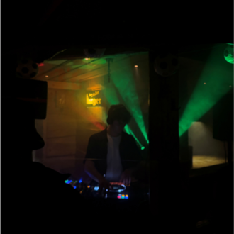 Ein DJ steht hinter einem Mischpult in einem dunklen Raum. Bunte Lichtstrahlen schaffen eine lebendige Atmosphäre.