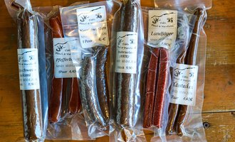 The image shows various types of sausages in transparent packaging. The sausages are differently colored and have labels with product information.