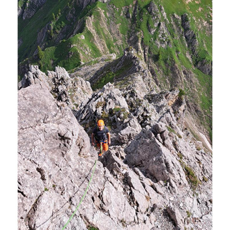 An impressive mountain landscape with steep cliffs and green meadows. A climber is on a rock face. | © stoamandl.at | Olli Sinz