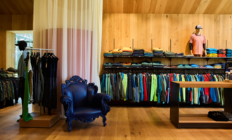 A modern store with a variety of clothing in vibrant colors. In the corner stands an elegant blue armchair.