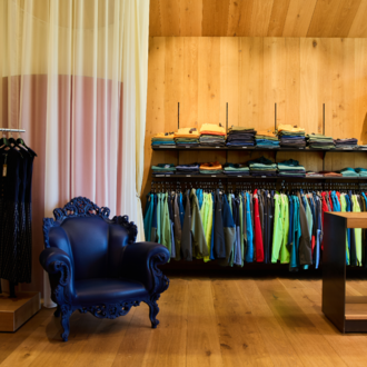 Ein modernes Geschäft mit einer Vielzahl von Kleidung in lebhaften Farben. In der Ecke steht ein eleganter blauer Sessel.