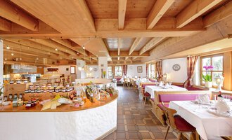 A cozy restaurant with a beamed ceiling and friendly atmosphere. Tables are set, and a buffet with various delicacies is visible. | © Alpengasthof Hörnlepass | Monschau Michael