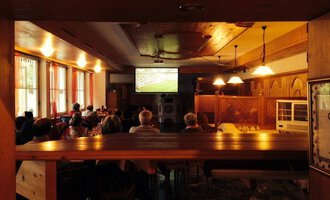 A group of people is sitting in a cozy room watching a soccer game on a large screen. The atmosphere is relaxed and friendly.