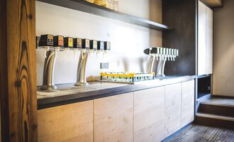 A modern drinks cabinet with multiple taps. The wooden shelves are designed in a simple and elegant way. | © Das Alphotel Hirschegg Hotel GmbH | Dominik Berchtold