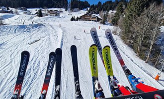 A ski lift ride over a snowy slope. In the foreground, several skis are visible, while in the background, the slope leads through a winter landscape. | © Austrian Ski- & Service Ranch | Trixi Leitner