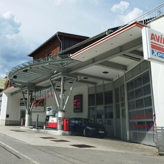 A modern gas station with a large canopy is located on a quiet street. In the background, residential buildings and a cloudy sky can be seen. | © Kleinwalsertal Tourismus | N. Lughammer