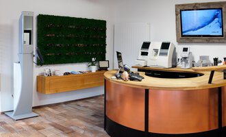A modern store with a reception counter made of wood and copper. Sunglasses hang on the wall, and there are technical devices for the customers. | © Blickfang | Michael Stumpe