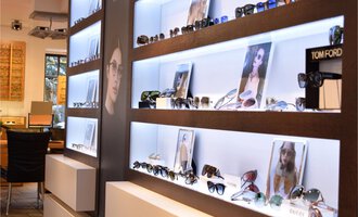 Ein stilvoller Raum mit einer Präsentation von Sonnenbrillen auf beleuchteten Regalen. Im Hintergrund sind Bilder von Models mit Brillen zu sehen. | © Bräuer Optik & Akustik | AlpenMedia-Design