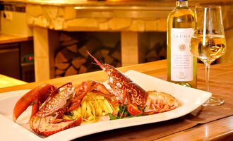 A delicious plate of fresh lobster and pasta, accompanied by a glass of white wine. In the background, a cozy restaurant atmosphere can be seen. | © Ristorante Trentino | Michael Monschau