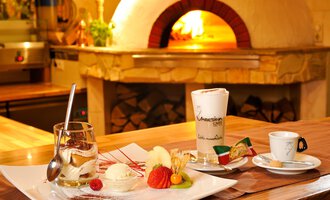 Ein köstliches Dessert auf einem elegante Teller, inklusive Eis und frischem Obst. Im Hintergrund ist ein Backofen sichtbar. | © Ristorante Trentino | Michael Monschau