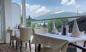 Ein eleganter Restaurantbereich mit weißen Tischen und Stühlen. Im Hintergrund sind grüne Berge und ein blauer Himmel zu sehen. | © Ristorante Trentino | Dietmar Jochum