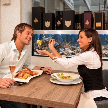Ein Paar sitzt in einem eleganten Restaurant und genießt ihr Essen. Sie lächeln sich an und scheinen eine gute Zeit zu haben.