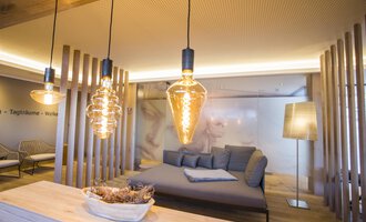 A modern living room with stylish light sources and a cozy sofa. The walls are bright and the space has a relaxed atmosphere. | © Genuss- & Aktivhotel Sonnenburg | Frank Drechsel