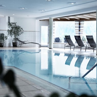 A bright indoor pool with loungers and plants. The room is designed to be modern and inviting. | © Hotel Birkenhöhe