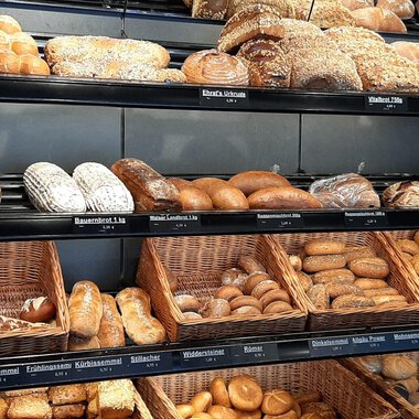 A shelf full of fresh rolls and breads in various shapes. The selection ranges from seed rolls to classic breads. | © Ehrat´s Backmanufaktur | Veronika Senn