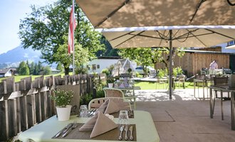 Eine gemütliche Terrasse mit Tischen und Sonnenschirmen. Im Hintergrund sind Bäume und eine malerische Landschaft zu sehen. | © Alexander Kaiser