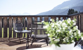 Eine gemütliche Terrasse mit modernen Stühlen und einem Blick auf die Berge. Im Vordergrund steht ein Topf mit grünen Pflanzen. | © Alexander Kaiser