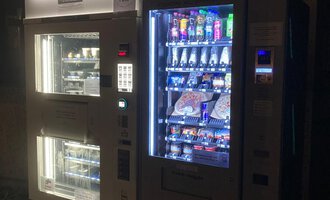 A vending machine in the dark with a variety of snacks and drinks. The machine glows and offers a colorful selection for customers.