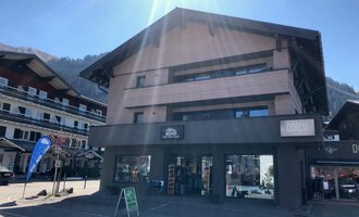 Ein modernes Gebäude mit mehreren Stockwerken, das eine Geschäftsfassade hat. Es befindet sich in einer malerischen Alpendorf-Umgebung. | © Sport Hilbrand GmbH