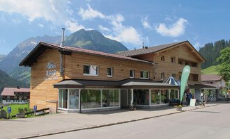 A modern wooden building in a picturesque mountain landscape. The clear skies and surrounding mountains give the place an inviting character. | © Sport Hilbrand GmbH