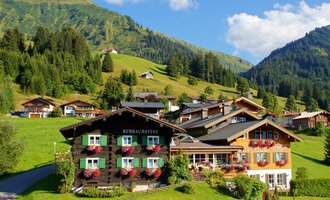 A picturesque landscape with traditional houses in the mountains. Lush green meadows and forests surround the buildings. | © Alpenhof Jäger | Werbewind