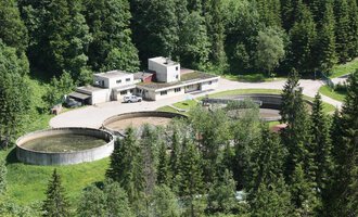 A modern wastewater treatment plant surrounded by dense forest. There are several large round basins and an administration building. | © Gemeinde Mittelberg