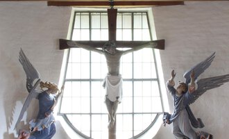 A beautiful church space with a cross and angels on the walls. The altar is adorned with flowers and has a bright, inviting atmosphere. | © Ev. Kirche Kleinwalsertal