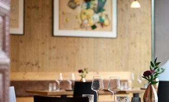 A cozy restaurant with wooden decor and stylish tables. On one table, there are glasses and a small flower vase. | © La Vallée | Annette Sandner