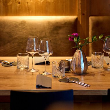 Ein schön gedeckter Tisch in einem gemütlichen Restaurant. Er ist mit Gläsern, Besteck und einer Vase mit Blumen dekoriert. | © La Vallée | Annette Sandner