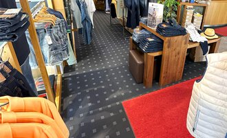 A well-organized clothing store with various textiles and accessories. The wooden floor and warm lighting create an inviting atmosphere. | © Moosbrugger Mode e.U.