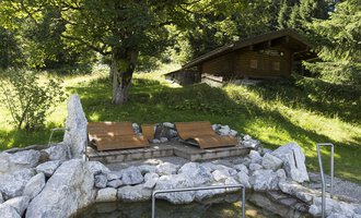 A quiet place with an outdoor sauna and loungers, surrounded by nature. In the background, there is a wooden house among the trees. | © Kleinwalsertal Tourismus | Oliver Farys