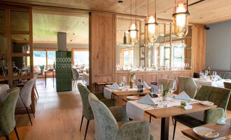 A modern restaurant with wooden decor and elegant tables. The space is bright and inviting, with cozy chairs and stylish lamps. | © Almhof Rupp | Lukas Kind