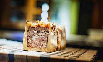 A piece of meat pie, beautifully presented on a wooden board. The pie has a light brown color with a decorative surface.