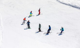 Eine Gruppe von Skifahrern steht auf einer verschneiten Piste. Der Himmel ist klar und die Sonne scheint. | © Skischule Bödmen-Baad GmbH