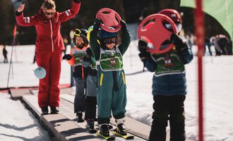 Eine Skischule für Kinder im Schnee. Die Kinder tragen Helme und halten Skischilder, während sie sich auf die Piste vorbereiten.