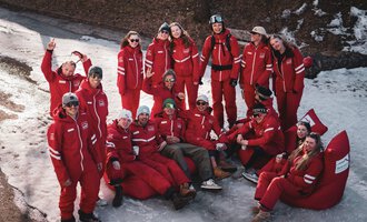 A group of people in red overalls happily poses in the snow. They stand and sit together in a relaxing atmosphere.