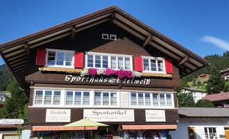 A traditional wooden house with red shutters and floral decorations. The clear sky and the surrounding mountains create an idyllic atmosphere. | © Sport Edelweiß | N. Lughammer