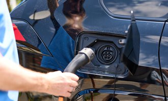 Eine Person lädt ein Elektroauto auf. Das Auto hat eine schwarze Karosserie und das Ladegerät wird angeschlossen. | © Kleinwalsertal Tourismus | Oliver Farys