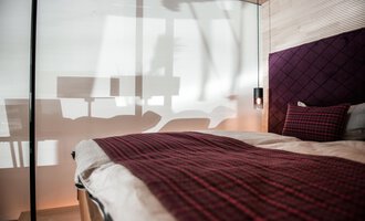A modern bedroom with a large bed and an elegant comforter. The soft shadows from the windows and furniture create a relaxed atmosphere in the room. | © Türtscher Die Schreinermanufaktur