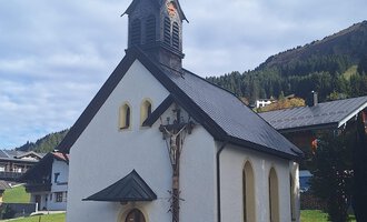 A small, white church with a pointed tower and wooden elements. In the background, green hills and trees are visible. | © Unterwestegg-Kapelle Maria Hilf | Tanja Ritsch