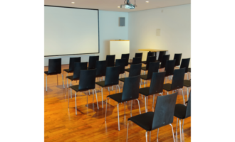 A modern seminar room with many black chairs in rows. On the wall, there is a screen for presentations.