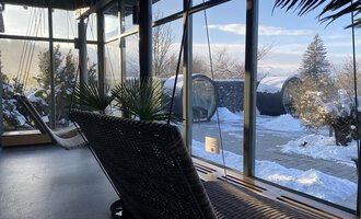 A cozy room with swings and large windows overlooking a snowy landscape. The indoor plants create a relaxed atmosphere. | © WONNEMAR Sonthofen | Julia Sondergelt