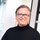 A man with brown hair, glasses, and a black turtleneck sweater, smiling kindly in front of a light-colored wall. | © Kleinwalsertal Tourismus eGen