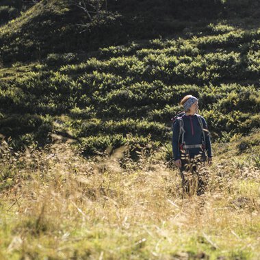 A lone hiker in autumn in the Black Forest, surrounded by green hills and dry grass | © Kleinwalsertal Tourismus eGen • Photographer: Andre Tappe