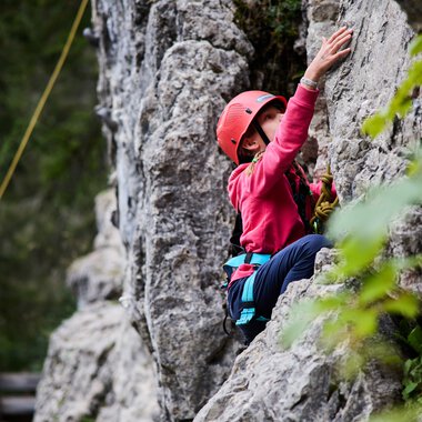 Kind beim Klettern in einem Klettergarten, mit Helm und Klettergurt, in der Natur, während eines Sommer-Trainings. | © Kleinwalsertal Tourismus eGen • Fotograf: Oliver Farys