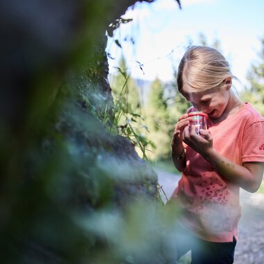 Ein junges Mädchen beim Naturforscherabenteuer im Kleinwalsertal, das eine Insektenkamera in der Hand hält und die Natur um sich herum erkundet. | © Kleinwalsertal Tourismus eGen • Fotograf: Oliver Farys