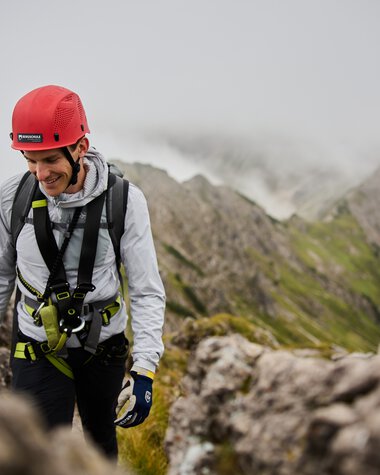 Abenteuerliche Klettertour auf einem Berg mit einem lächelnden Kletterer in Kletterausrüstung und Helm. | © Kleinwalsertal Tourismus eGen • Fotograf: Oliver Farys