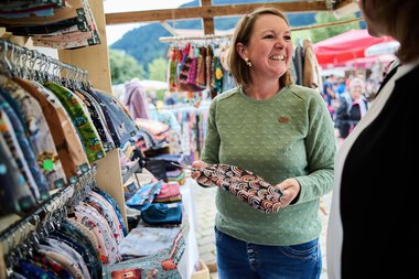 Woman selling handcrafted fabrics at a summer market stall in Kleinwalsertal. | © Kleinwalsertal Tourismus eGen • Photographer: Oliver Farys