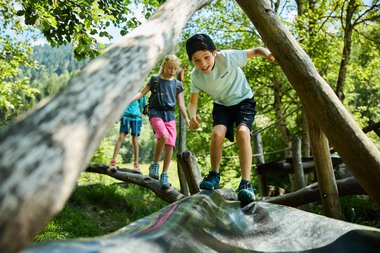 Children playing on a wooden bridge in the forest, laughing and exploring nature in Kleinwalsertal. | © Kleinwalsertal Tourismus eGen • Photographer: Oliver Farys