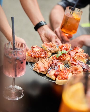People at a summer event in Kleinwalsertal serving pizza and drinking cocktails. | © Kleinwalsertal Tourismus eGen • Photographer: Oliver Farys